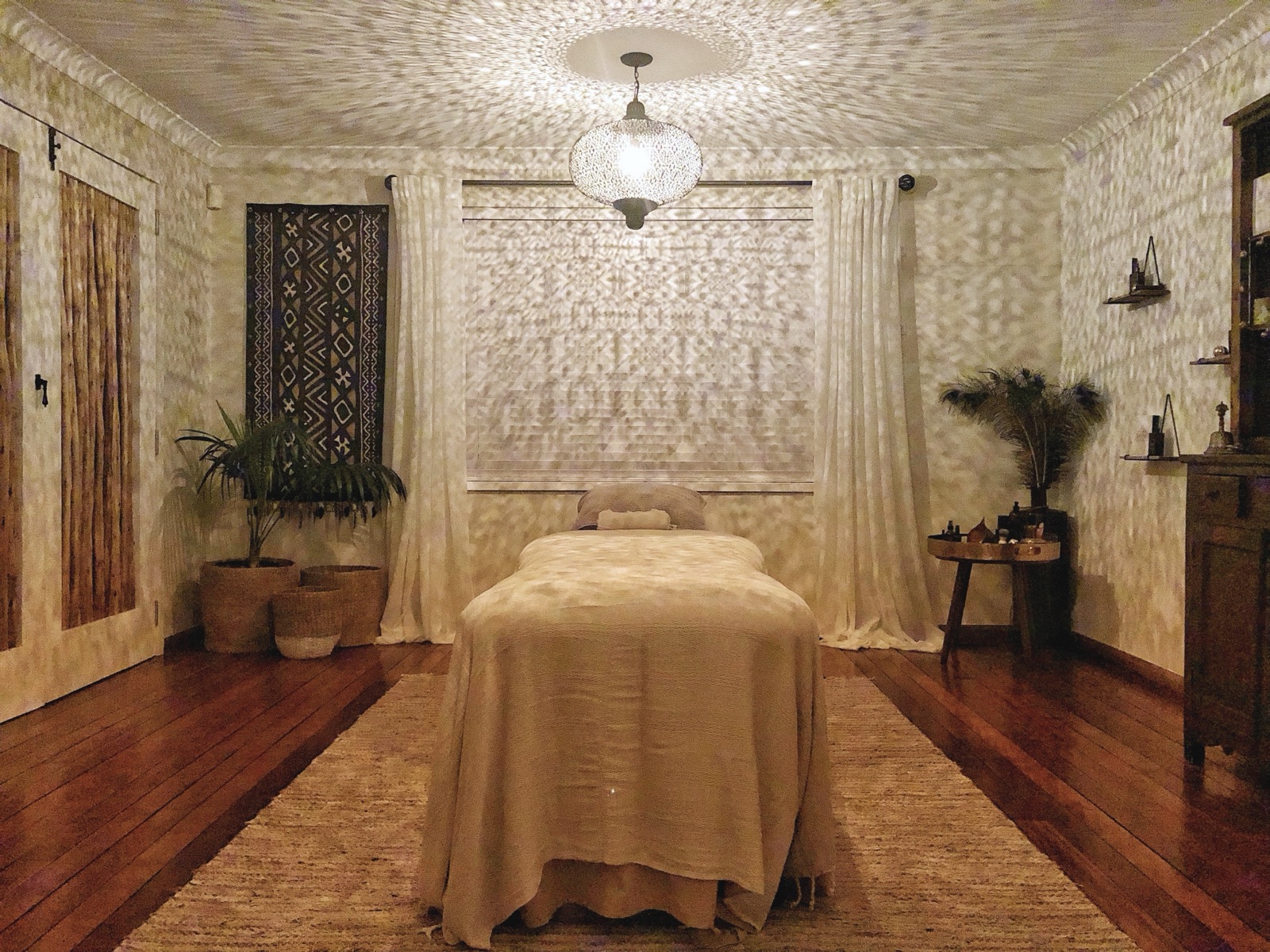 The Sacred Space treatment room, softly lit with a lantern, linen-draped massage table and plants